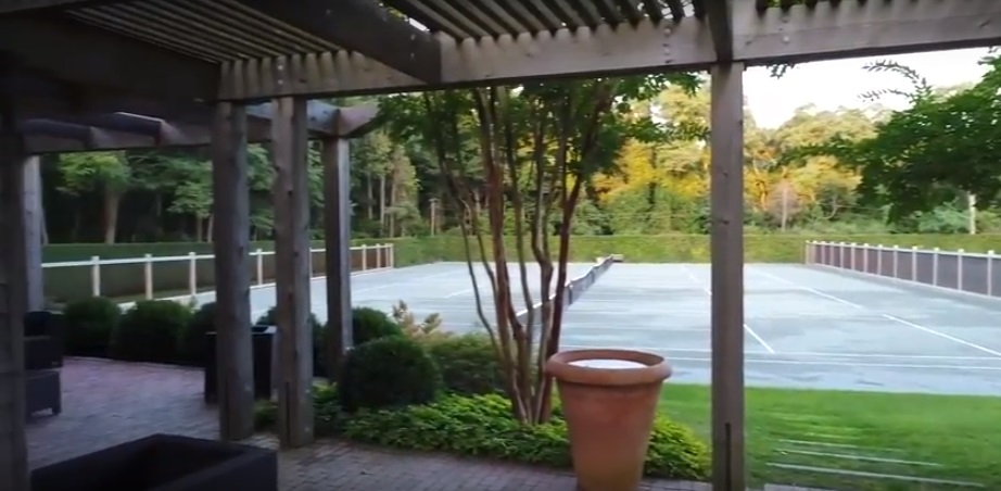 Manicured hedges and shaped evergreens surrounding a private tennis court.